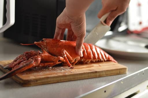 cutting up a cooked lobster with a knife on cutting board